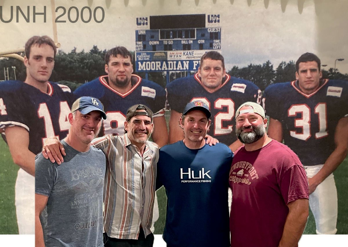 Four men posing in fronof a large "UNH 2000" mural featuring football players on Mooradian Field.