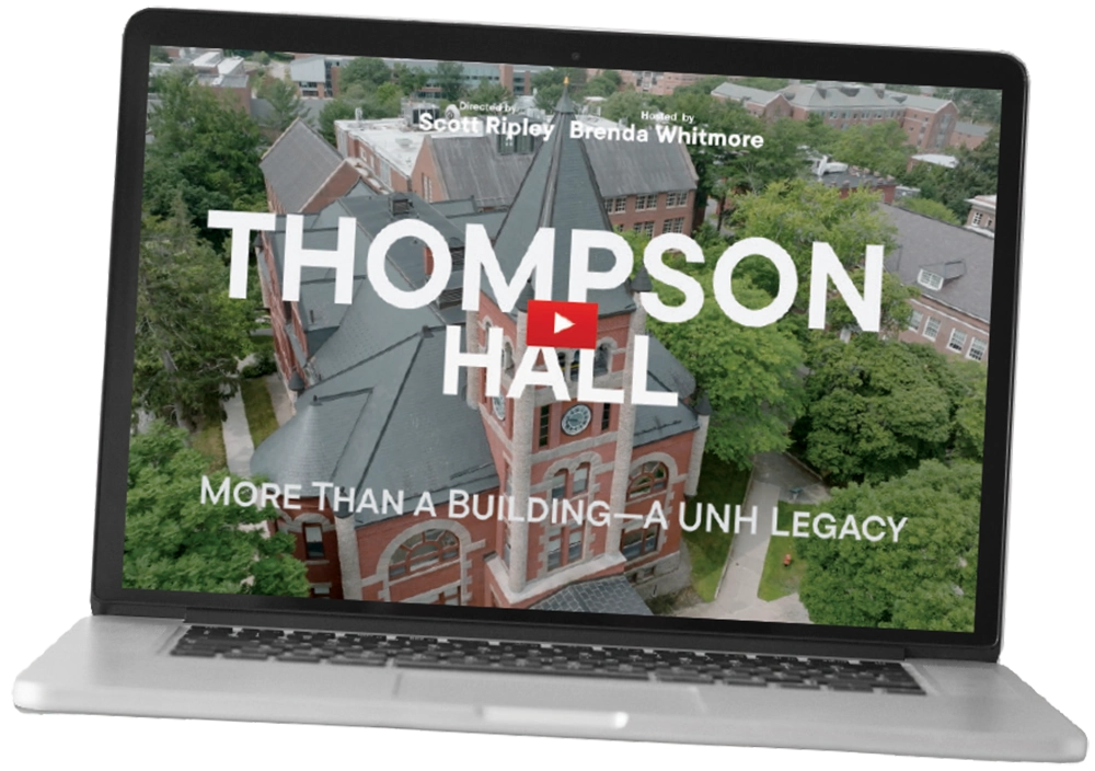A laptop screen displays a video titled "Thompson Hall: More Than a Building—A UNH Legacy" featuring an aerial view of the hall.