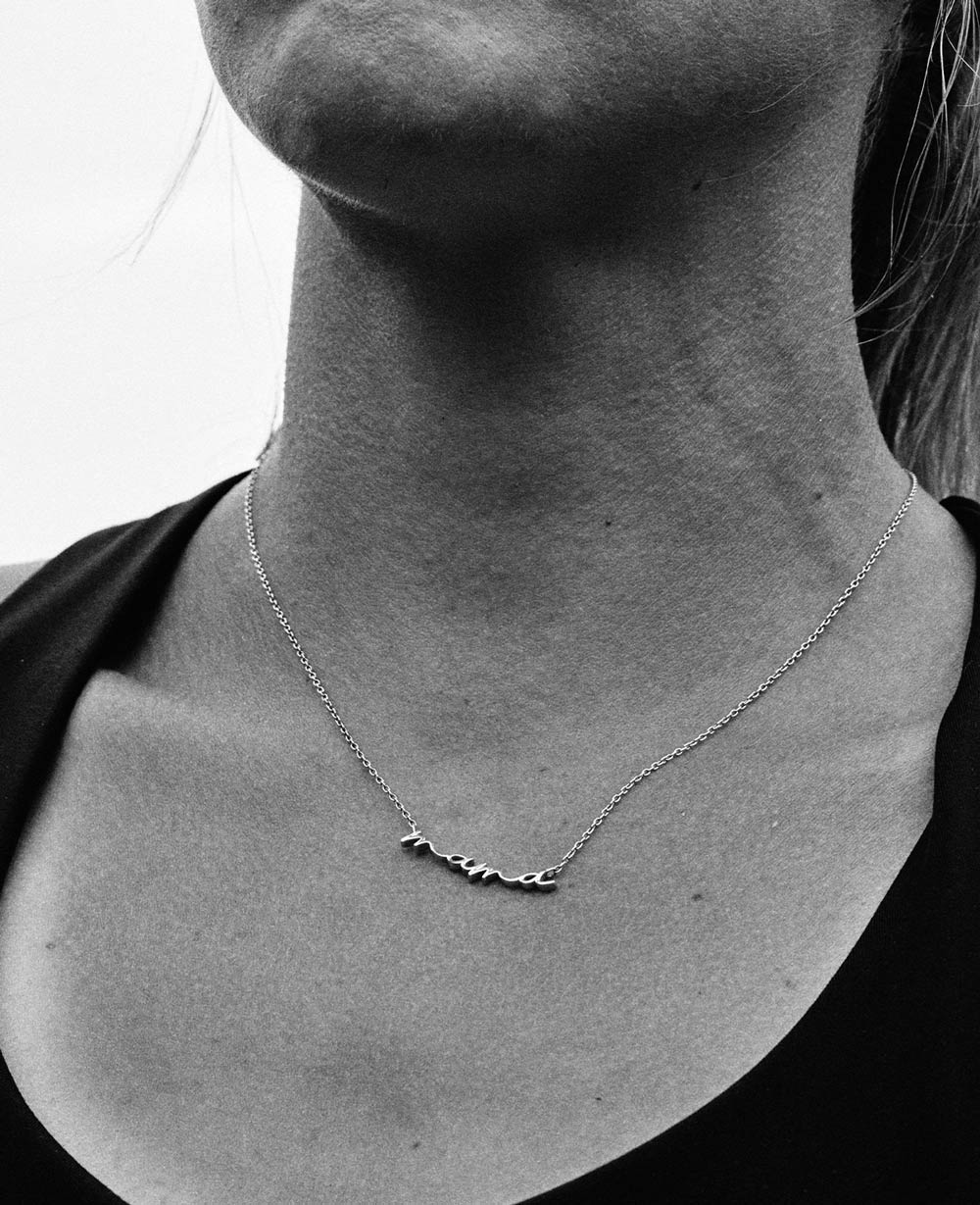 A black and white close-up of Elle Purrier St. Pierre’s neck. She wears a thin chain necklace with a script pendant that reads “mama.”