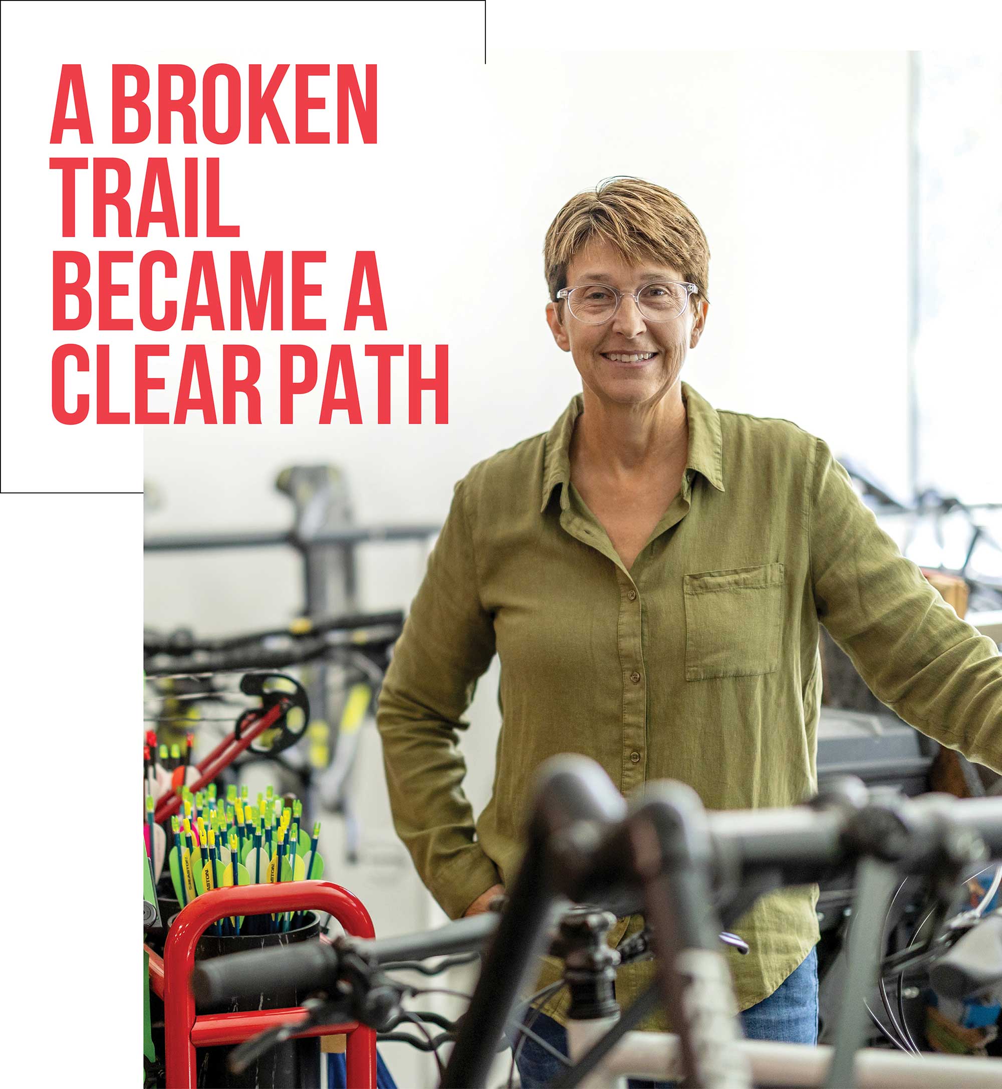 Woman standing in a workshop surrounded by bicycles and equipment, accompanied by bold red headline text reading "A broken trail became a clear path."