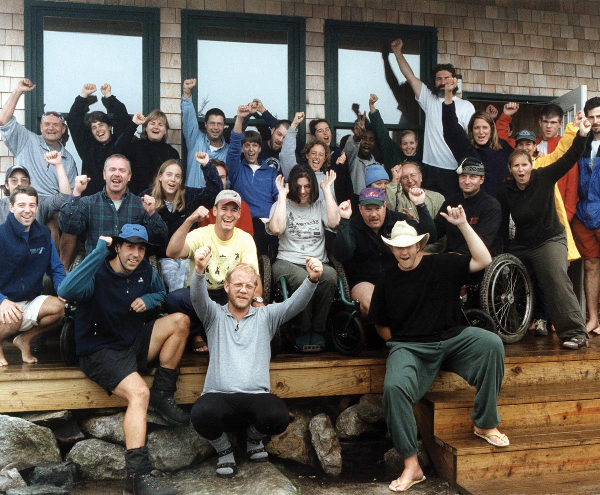 Group of active adults and wheelchair users cheering and celebrating on a outdoor wooden porch.
