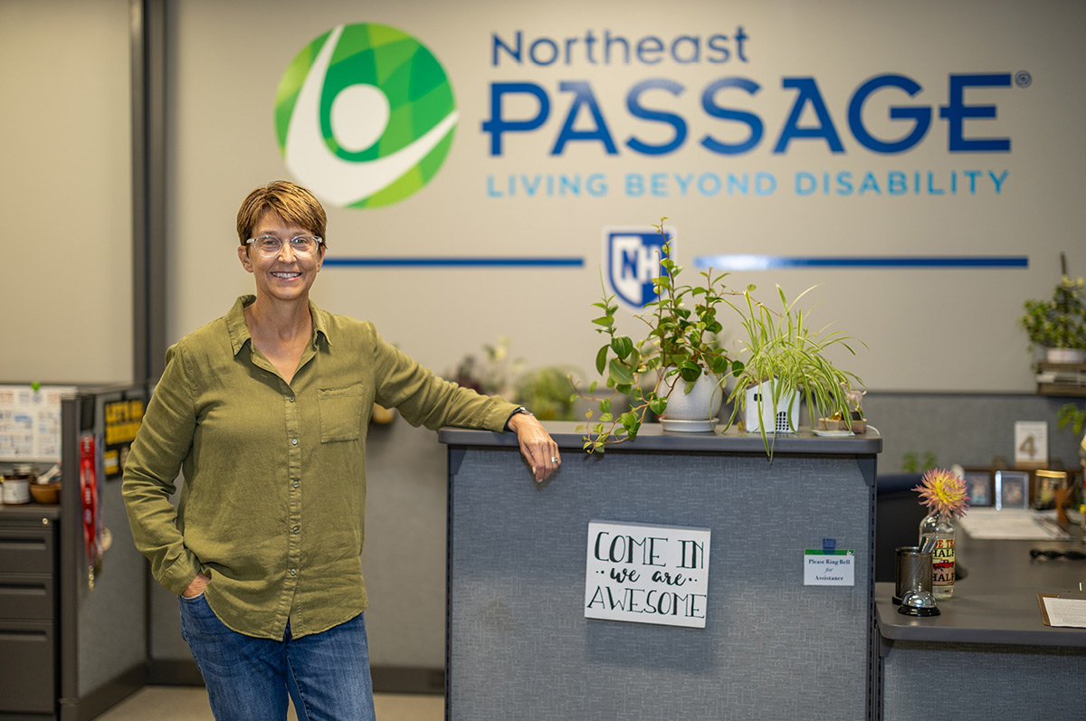 Woman standing in an office in front of a Northeast Passage company logo wall.