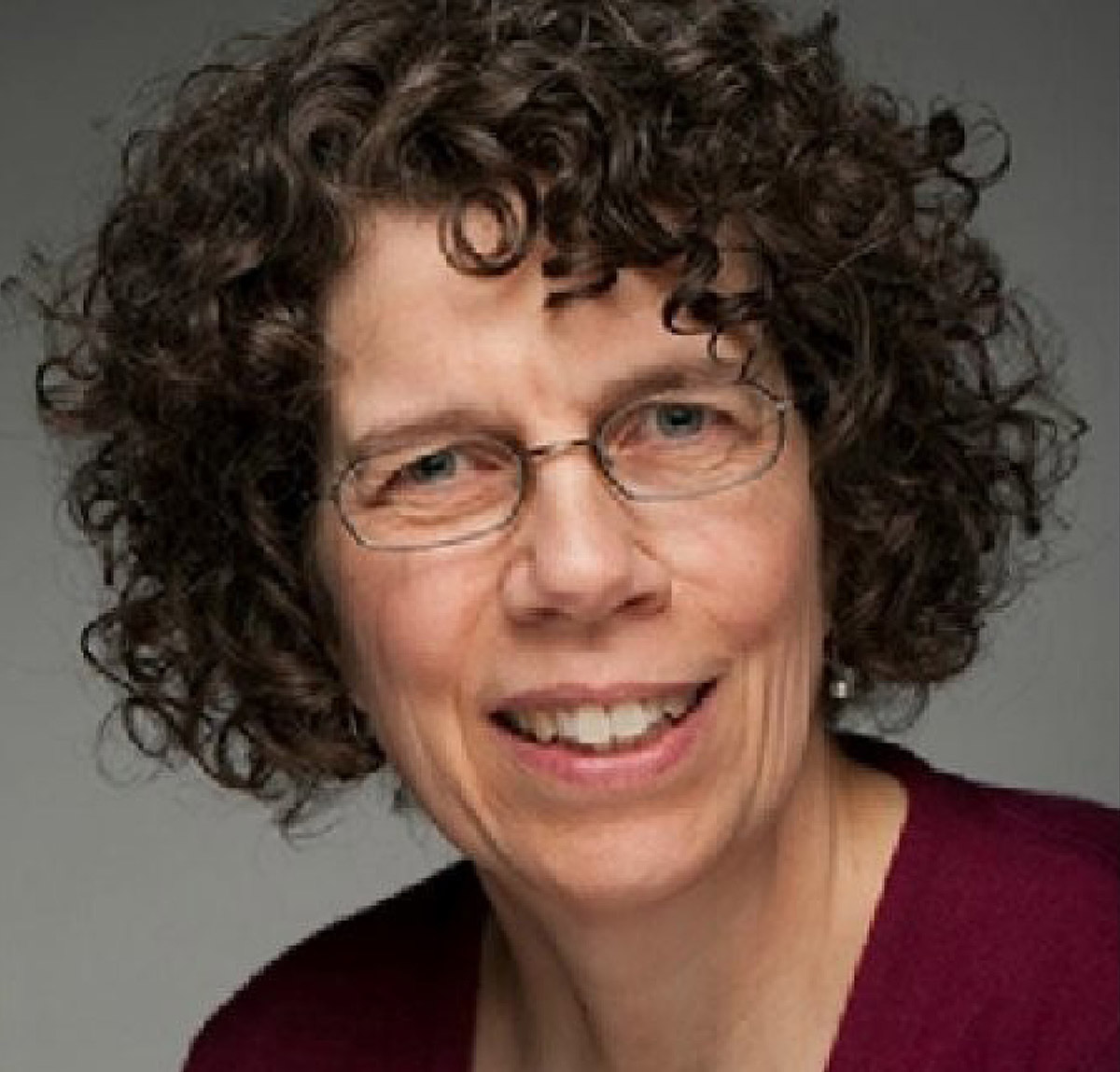 Headshot of Virginia “Ginny” Stuart smiling with curly dark hair and glasses.