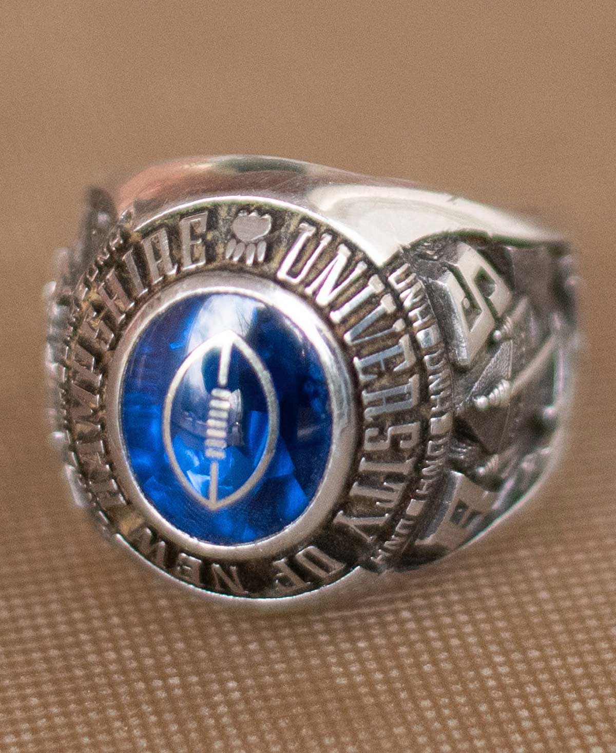 Silver class ring with a blue stone depicting a football for the University of New Hampshire.
