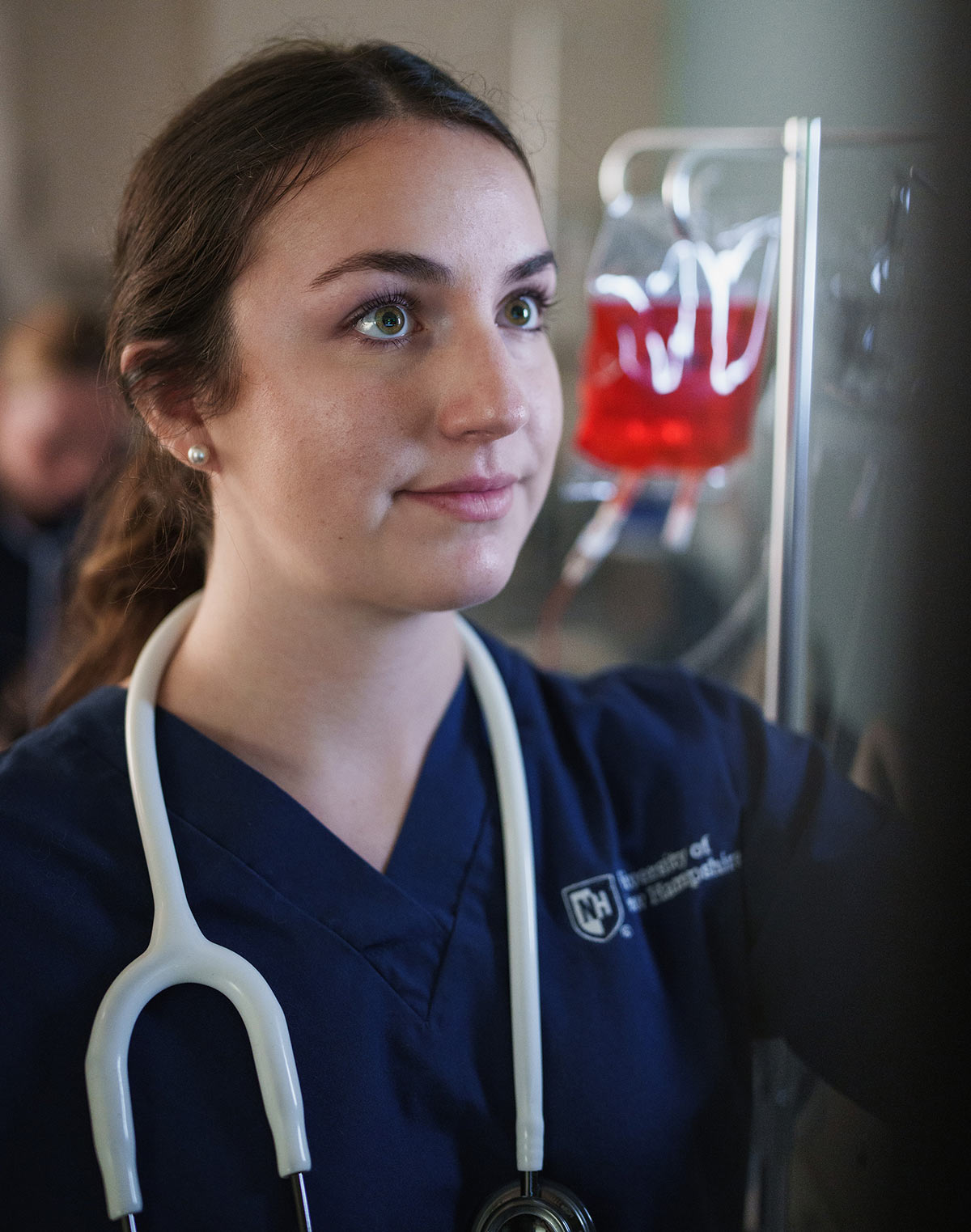 Female nursing student in scrubs with a stethoscope checking medical equipment.