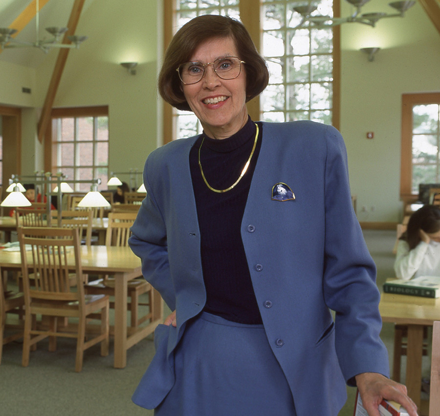 A portrait of Joan Leitzel smiling inside a spacious campus library setting.