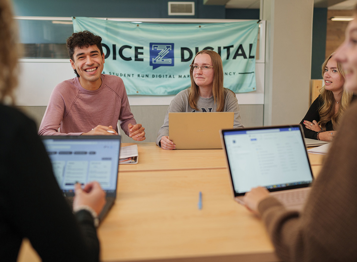 Four students sitting around a table with laptops during a digital marketing agency meeting.