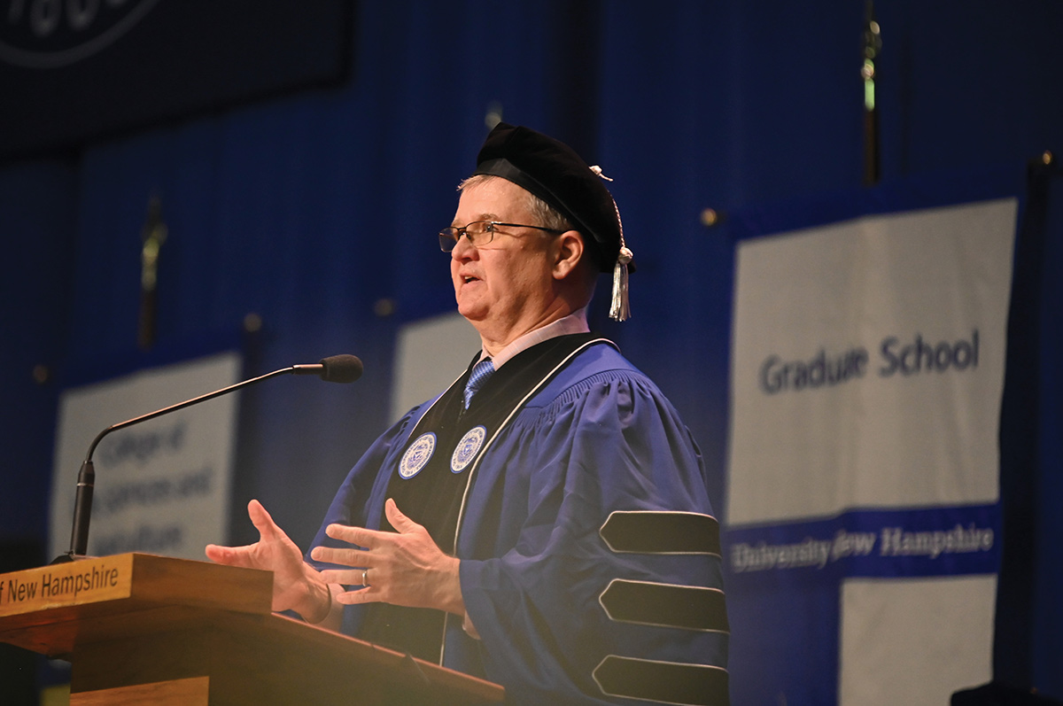 Speaker in academic regalia delivering a commencement address at a podium.
