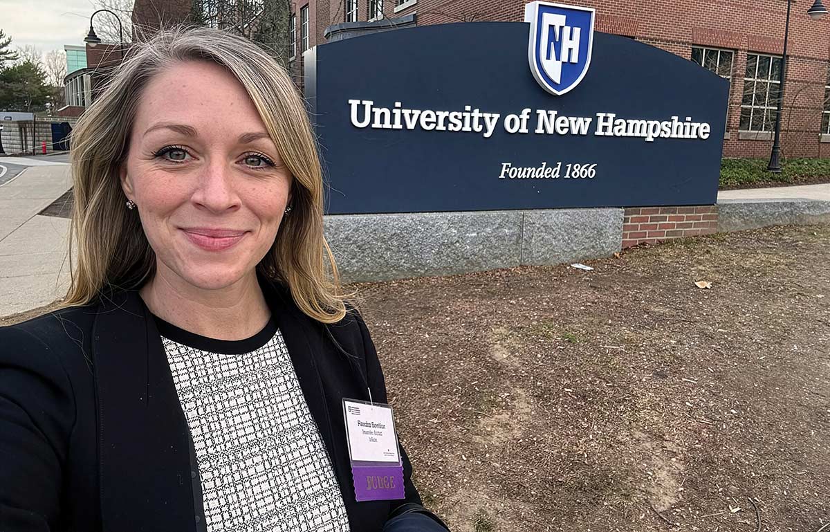 Woman taking a selfie in front of the University of New Hampshire sign.