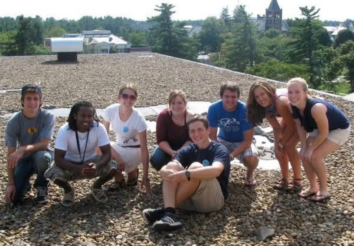 Group of university students posing together sitting and crouching on a gravel rooftop.