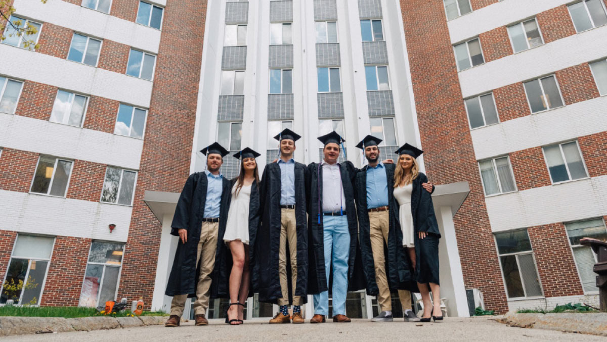 Six university graduates in caps and gowns posing in front of Stoke Hall.