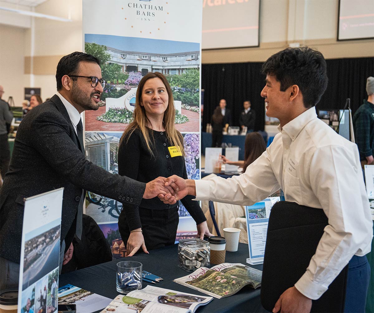 A student shaking hands with a representative across a Chatham Bars Inn display table at a career fair.