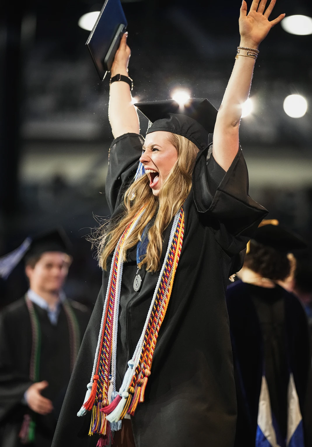 A University of New Hampshire graduate cheers with both arms raised while holding her diploma during commencement.
