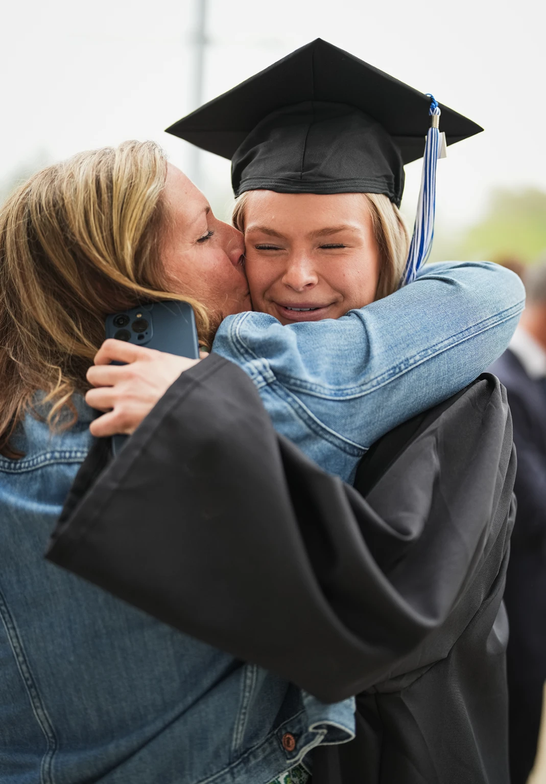 A woman embraces and kisses a smiling University of New Hampshire graduate on the cheek after commencement.