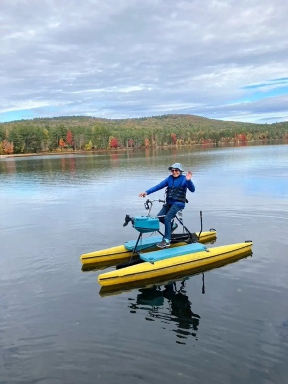 Joan Lamson ’49 rides a yellow pedal-powered watercraft on Pleasant Lake, with wooded hills in the background.