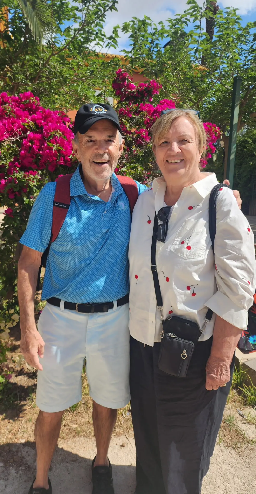Philip and Ann Grandmaison, both ’73, stand together outdoors among flowering plants.