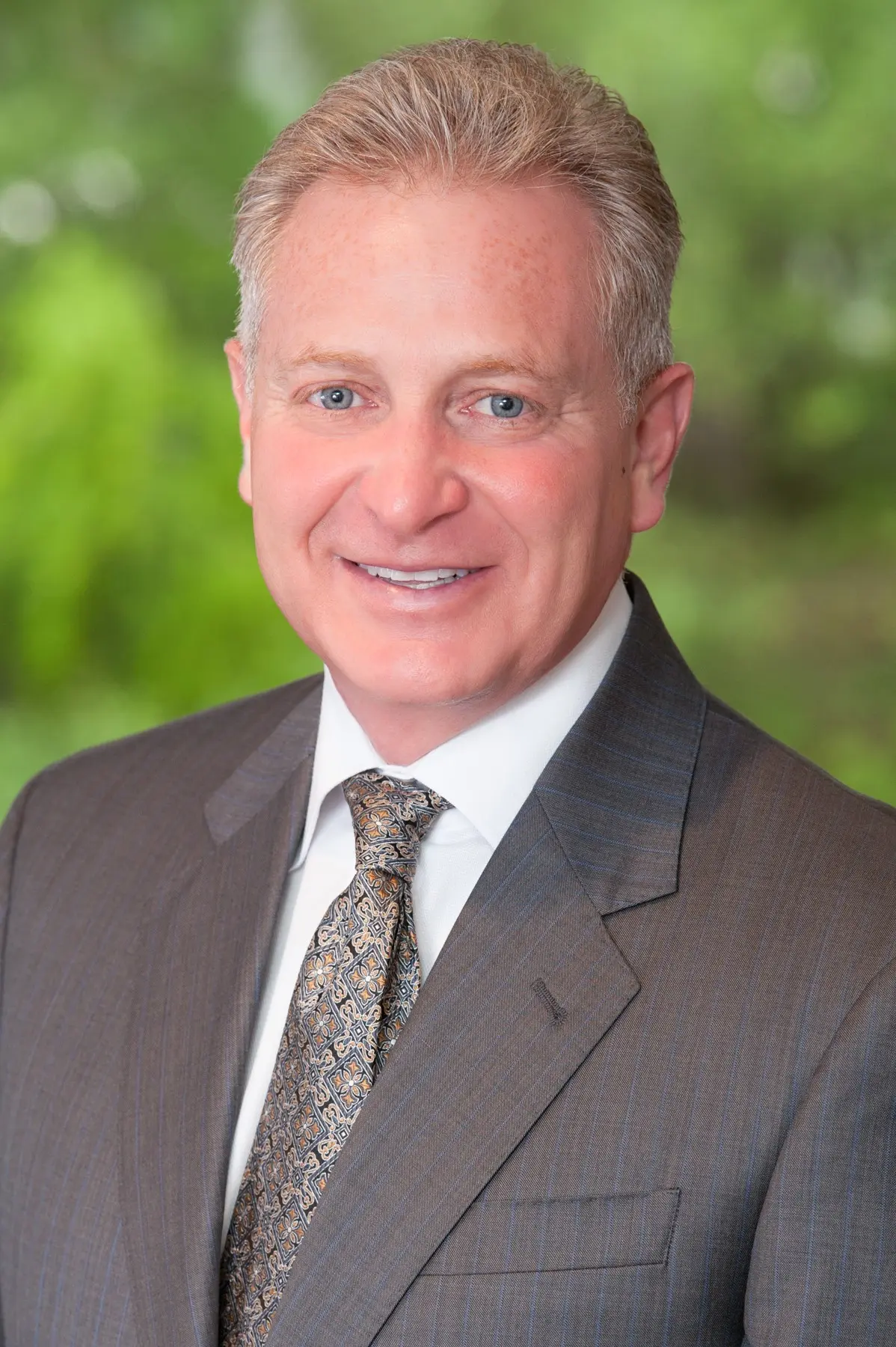 Barry Zimmerman ’86 smiles for a professional portrait in a suit and patterned tie.