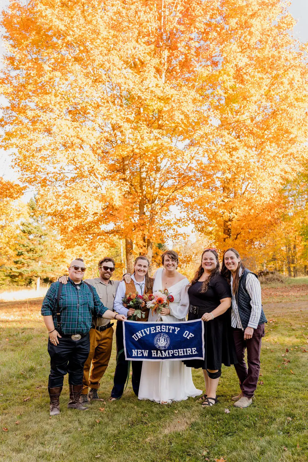 Kam Jamison ’10 and Leanne McGaughey-Rubchinuk ’15 celebrate their wedding outdoors with a group of friends beneath autumn foliage.
