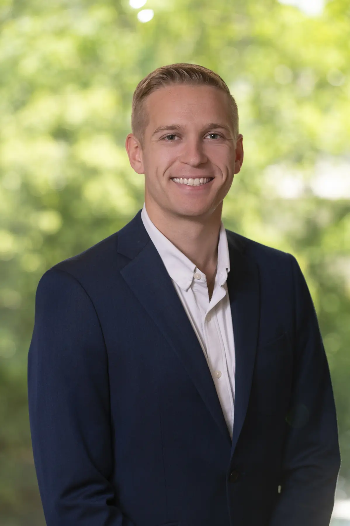 Professional portrait of Dylan Grocer ’20 smiling outdoors in a navy suit jacket and white shirt.