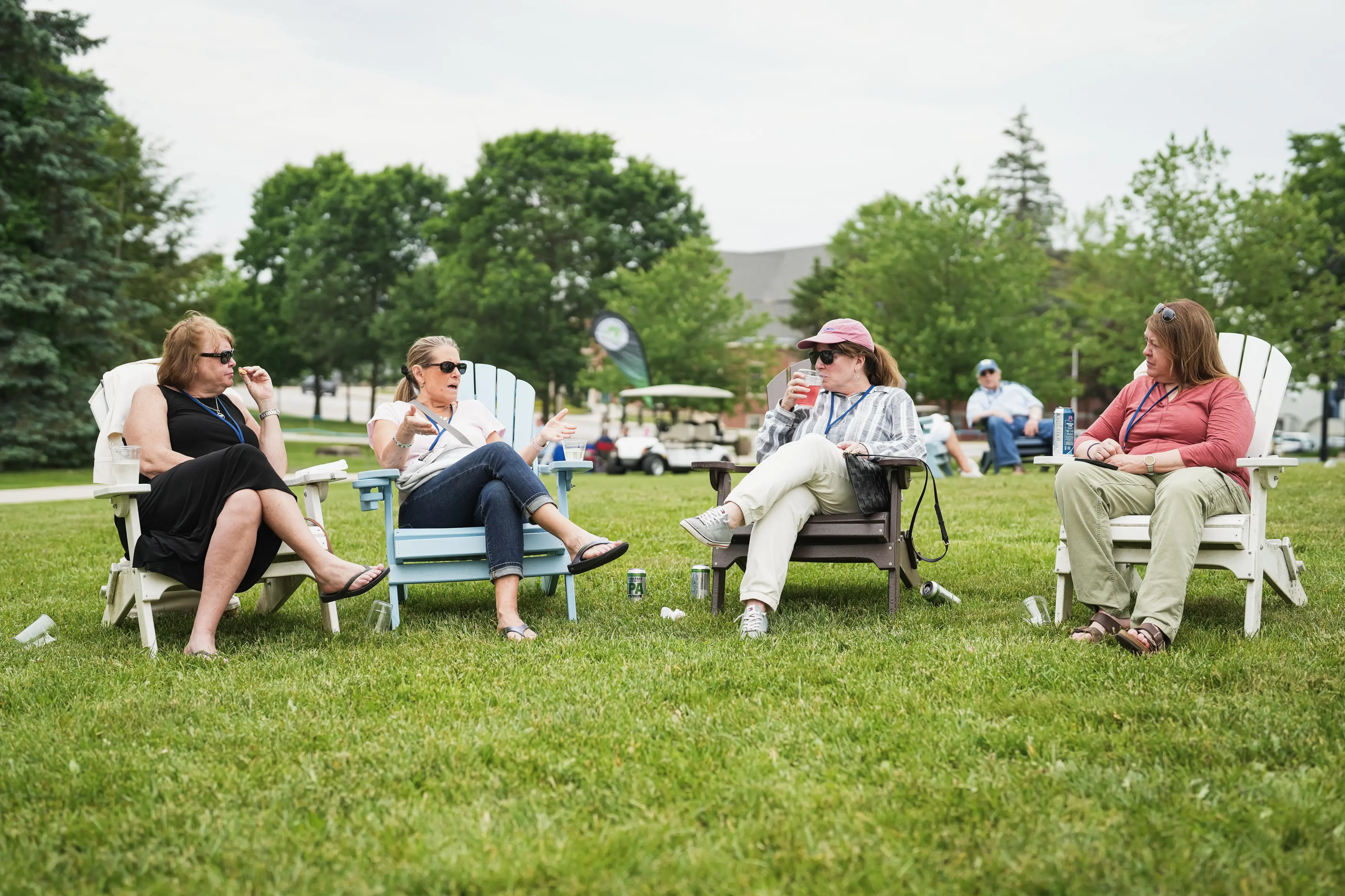 Four alumnae sit in Adirondack chairs talking together on a campus lawn during reunion weekend.