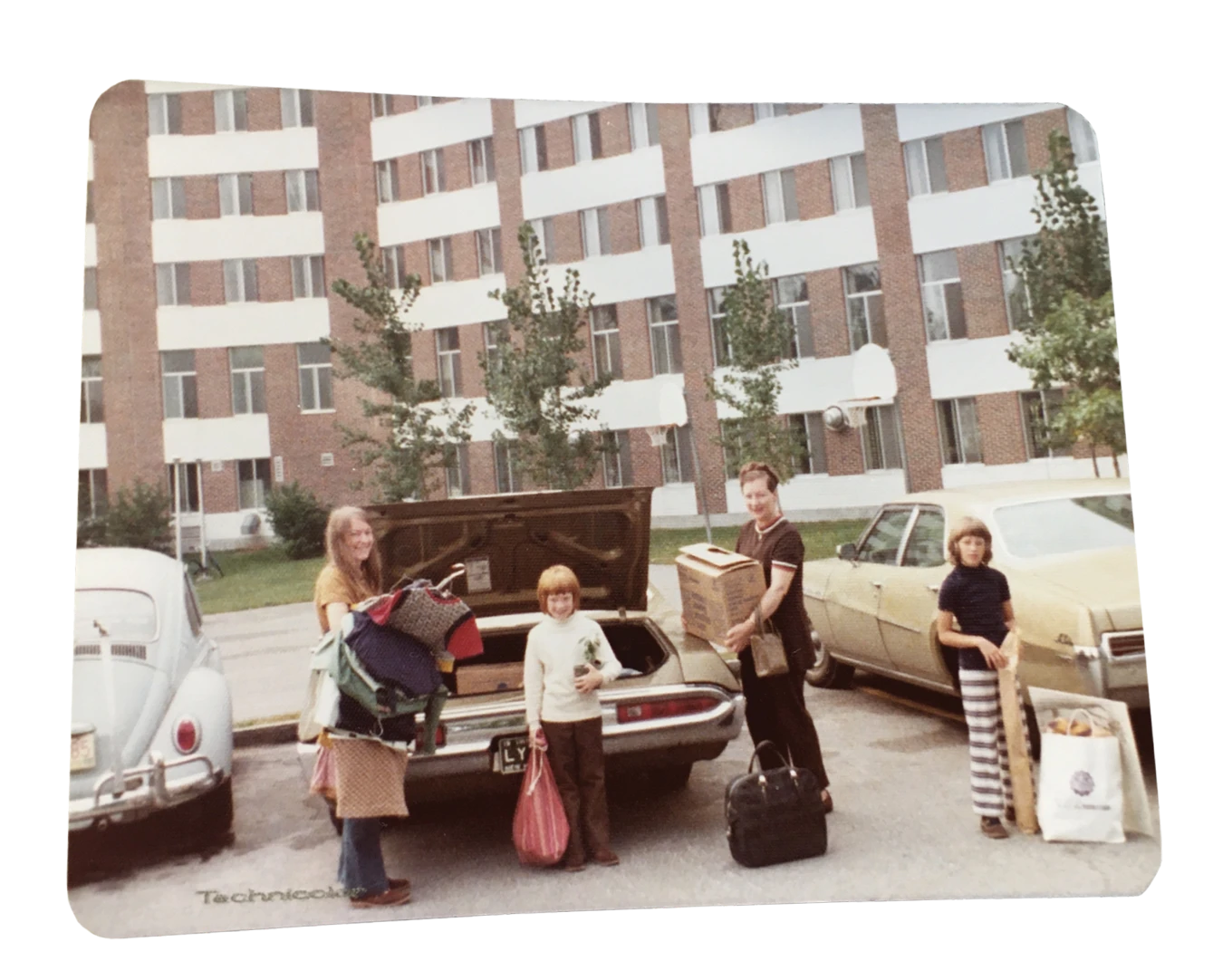 Archival photograph of a family unloading boxes, bags, and bedding from cars outside a university residence hall.