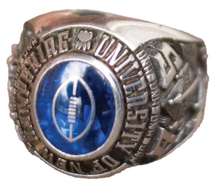 Close-up of a University of New Hampshire class ring with a blue stone and Wildcat emblem.
